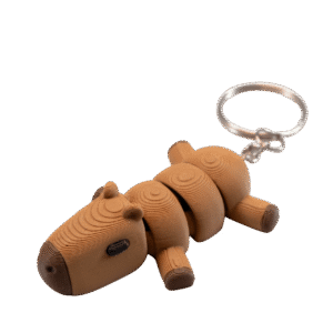 Kaprys – brelok kapibara z druku 3D leżący na boku. Beżowo-brązowa kapibara zbudowana z segmentów z widocznymi koncentrycznymi okręgami na powierzchni. Małe uszka, krótkie nóżki z ciemniejszymi stopkami, nos i oczy. Spokojna, relaksująca poza. Metalowe kółko do zawieszenia.