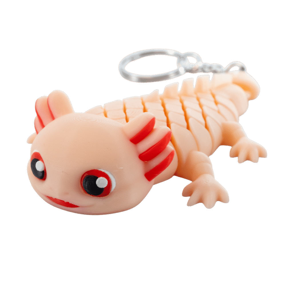 Saly – brelok aksolotl z druku 3D leżący na boku. Beżowo-pomarańczowa salamandra z wielkimi okrągłymi oczami, czerwonymi skrzelami na główce i czerwonymi paskami po bokach. Widoczne cztery małe łapki i metalowe kółko do zawieszenia. Delikatny uśmiech na pyszczku.