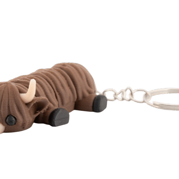 Futrzag – miniz brelok krowa highland z druku 3D - brązowa, włochata figurka w wersji mini z rogami i czarnymi kopytami, leżąca przy metalowym kółku do kluczy.
