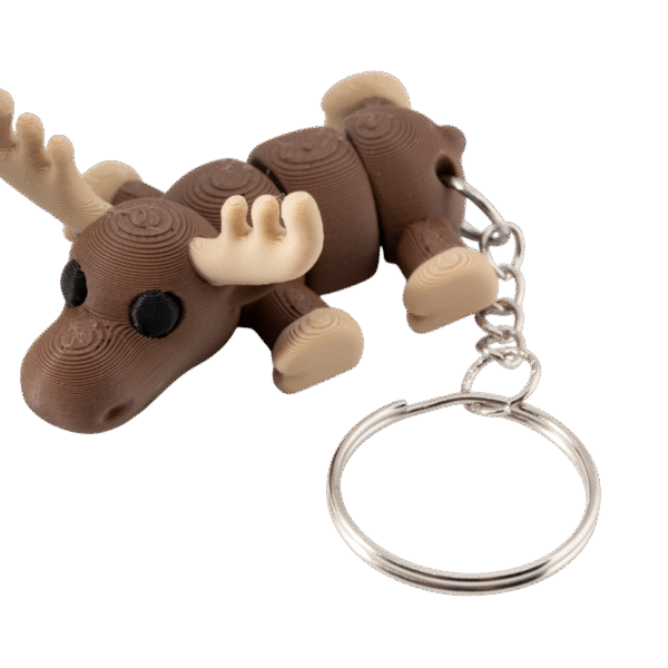 Brelok łoś z druku 3D w stylu miniz, w ciepłym brązowym kolorze, z dużymi kremowymi porożami i czarnymi oczami. Łoś leży w pozycji poziomej, z segmentowanym ciałem pozwalającym na ruch elementów. Do jego grzbietu przymocowany jest metalowy łańcuszek zakończony okrągłym, srebrnym kółkiem na klucze. Model ma gładką, warstwową fakturę charakterystyczną dla druku 3D.