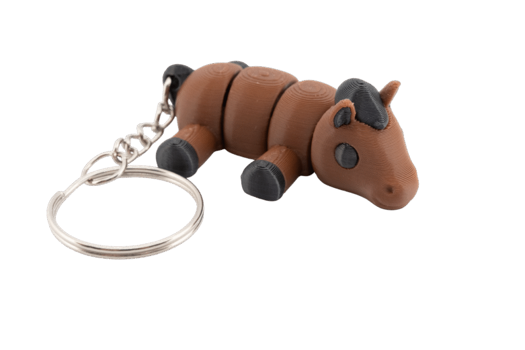 brelok koń z druku 3d w stylu miniz, mały brązowy konik o segmentowym ciele z czarną grzywą i kopytami, leżący przodem do obserwatora, z dużym metalowym kółkiem do kluczy po lewej stronie