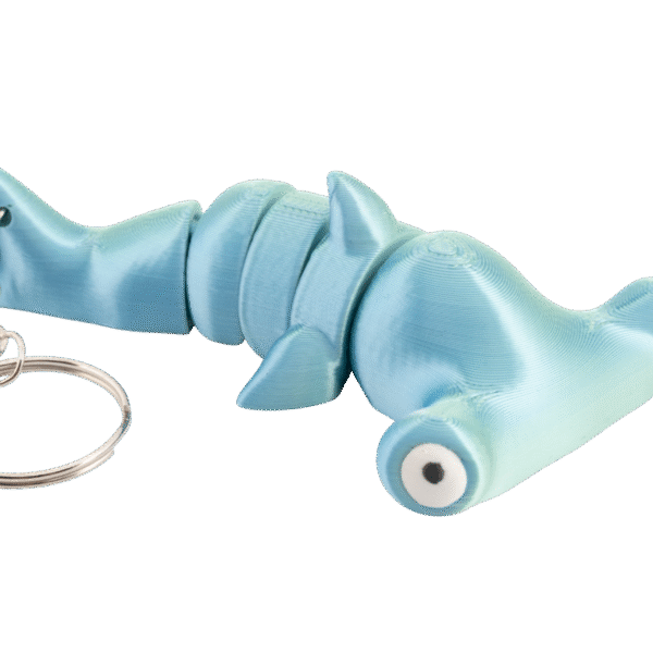 brelok rekin młot z druku 3d w kolorze jasnego turkusu, pokazany z boku w pozycji leżącej; ma segmentowane ciało z ruchomymi częściami, charakterystyczną szeroką głową młota, duże białe oczy z czarnymi źrenicami oraz metalowy łańcuszek i kółko do kluczy po lewej stronie