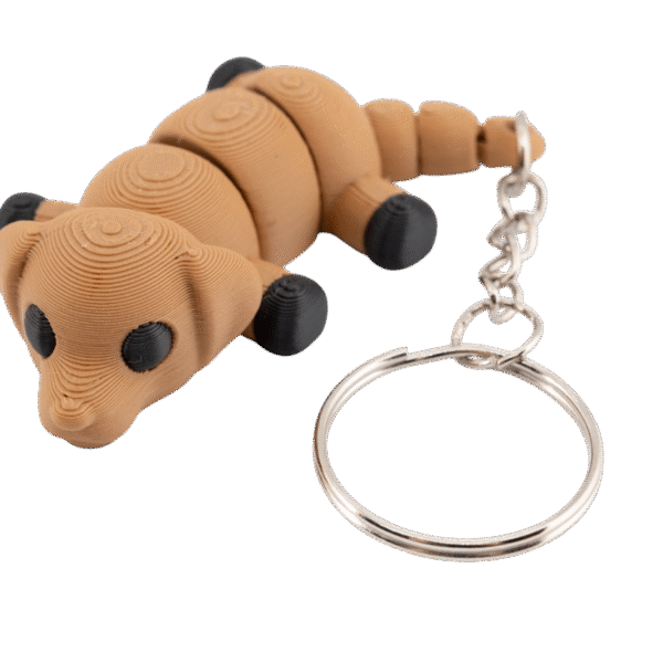 brelok piesek z druku 3d w kolorze jasnobrązowym, segmentowy miniz z czarnymi łapkami i oczami, leżący przodem z metalowym kółkiem do kluczy po prawej stronie
