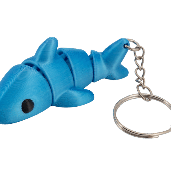 brelok rekin z druku 3d w intensywnie niebieskim kolorze, przedstawiający uroczego rekinka z dużą, gładką głową i okrągłym czarnym okiem, segmentowanym tułowiem z drobnymi, zaokrąglonymi płetwami po bokach oraz charakterystyczną płetwą ogonową; całość połączona z metalowym łańcuszkiem i kółkiem na klucze, leżąca na białym tle, w formie lekkiej, elastycznej zabawki-breloka