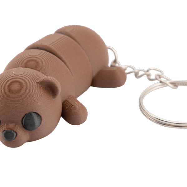 brelok miś z druku 3d w kolorze ciepłego brązu, przedstawiający leżącego misia o segmentowym, ruchomym korpusie; ma okrągłą głowę z małymi uszami, czarne oczy z delikatną teksturą warstw druku i mały czarny nosek, a z tyłu przymocowany jest metalowy łańcuszek z kółkiem do kluczy