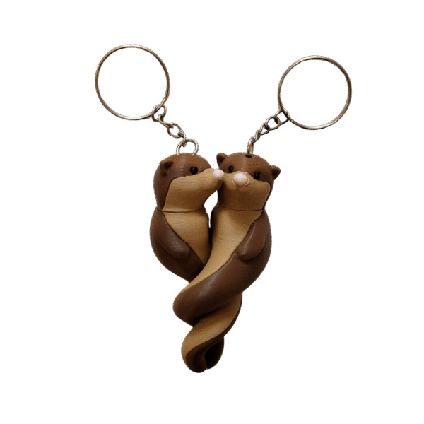Miłosny splot wydr to para breloków z druku 3D, brązowo-beżowe splecione zwierzątka z różowymi noskami i metalowymi kółkami